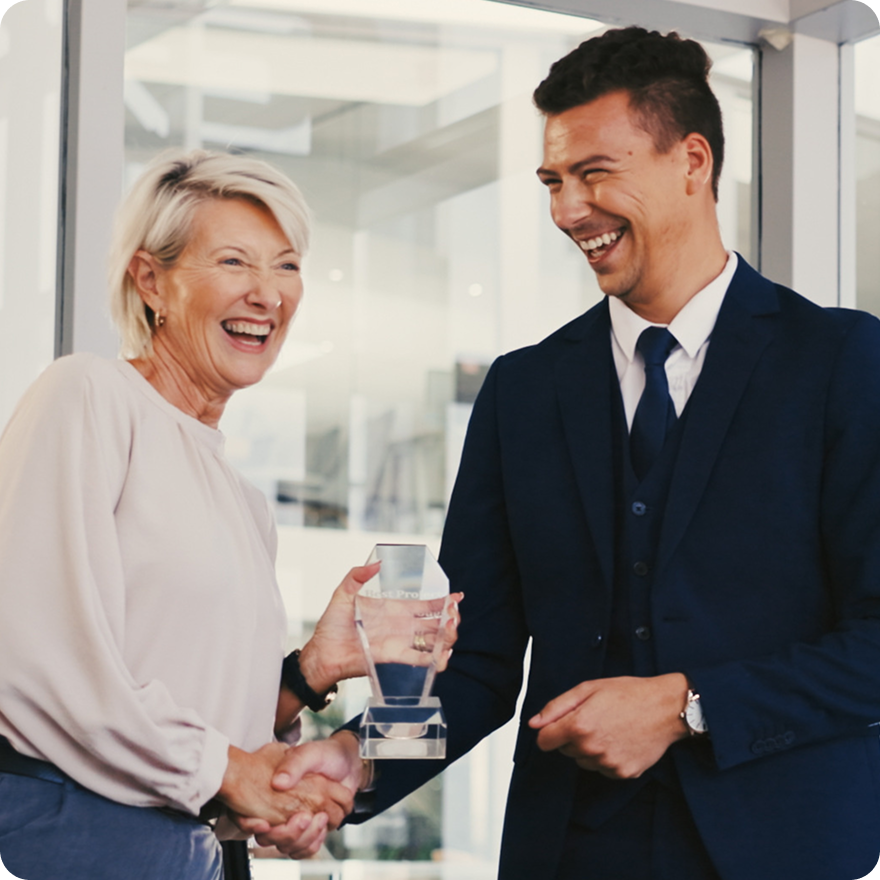 Smiling professionals exchanging a award in a modern office setting, celebrating achievement and recognition.